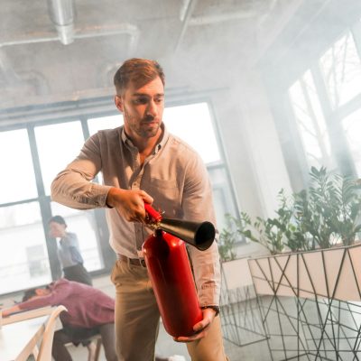 handsome businessman holding extinguisher in office with smoke near colleagues